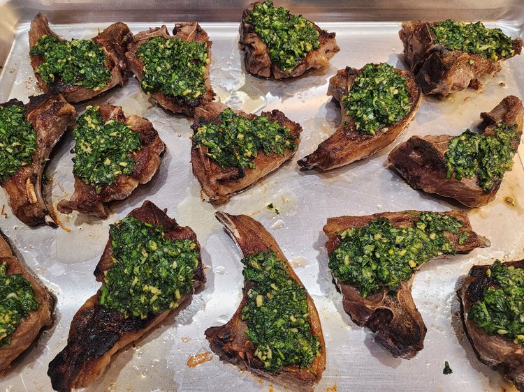 Grilled lamb chops topped with a vibrant green herb sauce, arranged neatly on a baking tray, showcasing a delicious recipe for a flavorful main dish.